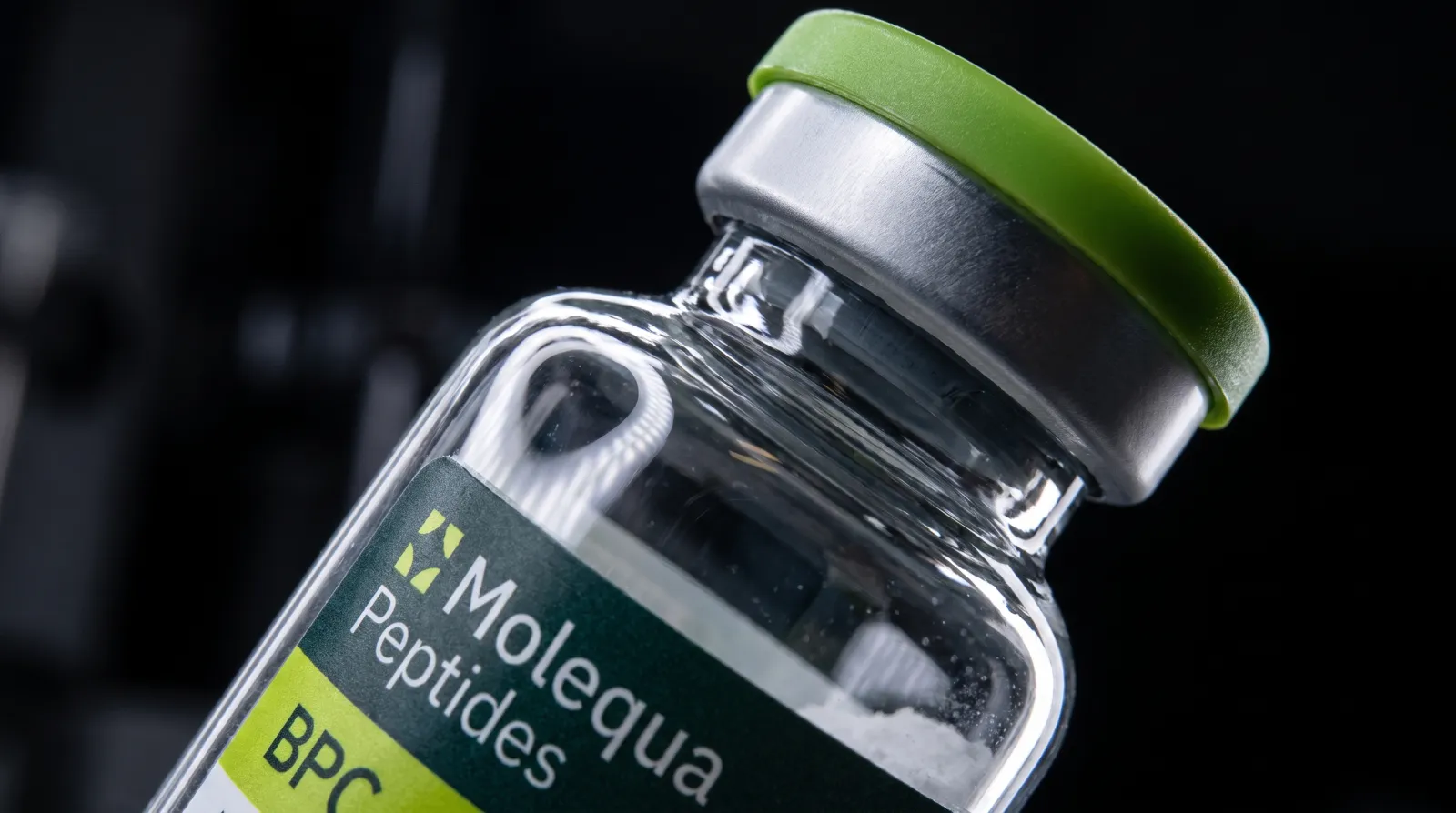 Detailní makro hrdla a zeleného uzávěru vialky s peptidem BPC-157 na tmavém pozadí